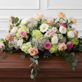 Casket spray with pastel roses, hydrangeas, and trailing greenery