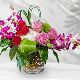 Pink and red roses with purple orchids in a glass vase