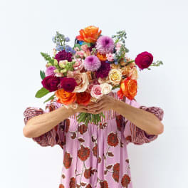 Person holding a colorful mixed bouquet of roses and other blooms