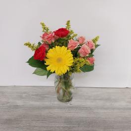 Small vase arrangement with yellow gerbera daisy, pink roses, and red carnations in a glass vase