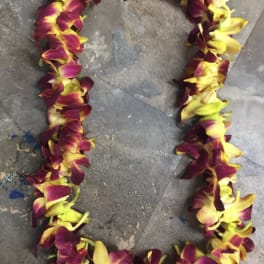 A lei made of purple and yellow orchid blossoms on a gray floor.