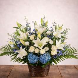 White lilies, roses, and blue hydrangeas in a wicker basket