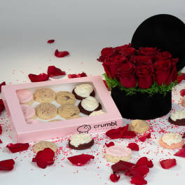 Red roses in a black hatbox beside a pink box of cookies