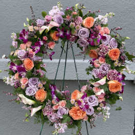 Circular floral wreath with roses, calla lilies, and orchids on a stand