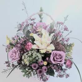 Lavender roses, cream lilies, and mixed blooms arranged in a white handled basket