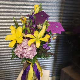 Yellow lilies and purple flowers in a glass vase with ribbon and glitter toppers