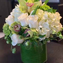 White roses, hydrangeas, and orchids in a green glass vase