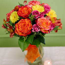 Bouquet of orange and pink roses with yellow daisies in a glass vase
