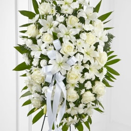 Standing spray of white lilies, roses, and carnations with a white ribbon on an easel.