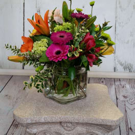 Mixed bouquet of orange lilies, pink gerbera daisies, and green mums in a glass vase