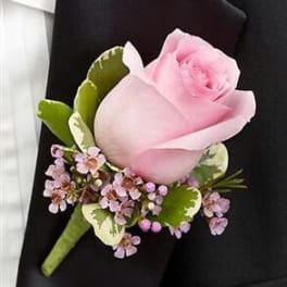 Pink rose boutonniere with tiny pink filler flowers pinned to a black suit lapel.