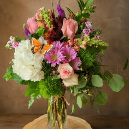 Mixed bouquet of pink and white flowers in a glass vase with a butterfly accent