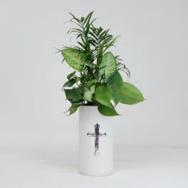Green foliage arrangement in a white vase with a cross emblem