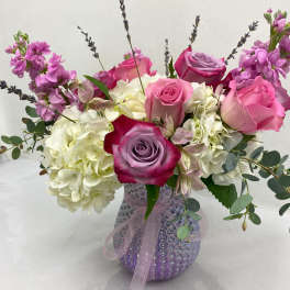 Pink and lavender roses with white hydrangeas in a textured lavender glass vase tied with ribbon