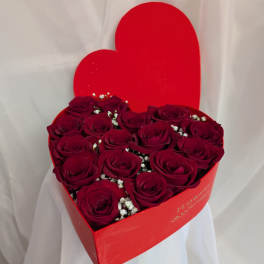 Heart-shaped red box filled with deep red roses and small white filler flowers