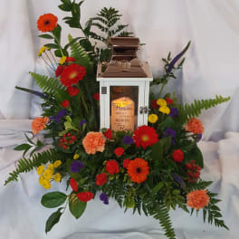 Floral funeral lantern arrangement with mixed bright flowers around a white lantern