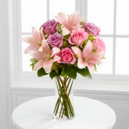 Pink lilies and roses arranged in a clear glass vase