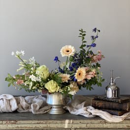 Mixed flower arrangement in a silver vase with peach, white, and blue blooms