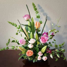 Tall floral arrangement with pink and peach roses and lilies in a black container