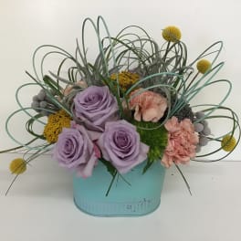 Lavender roses and pink carnations in a blue container with looping grass