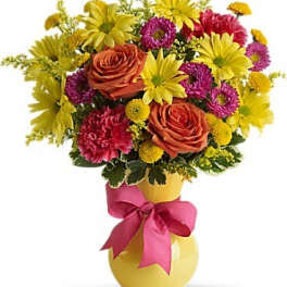 Colorful bouquet of roses, daisies, and carnations in a yellow vase with a pink ribbon.