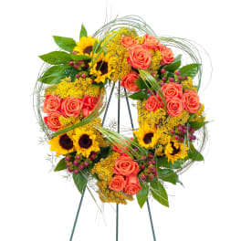 Circular floral wreath with orange roses and sunflowers on a stand