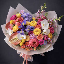 Colorful mixed bouquet with roses, orchids, and irises wrapped in pale paper