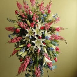 Tall floral spray with white lilies, pink blooms, and blue accents on a stand