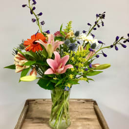 Mixed bouquet of lilies, gerbera daisies, and purple flowers in a glass vase