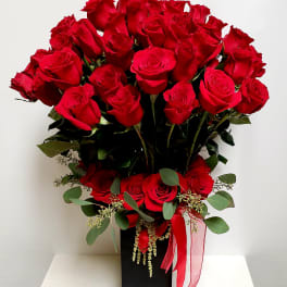 Red roses arranged in a black rectangular vase with a red ribbon