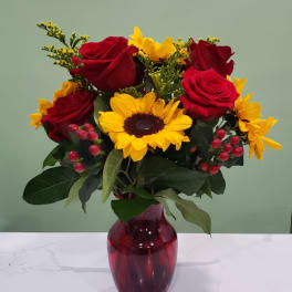Bouquet of red roses and yellow sunflowers in a red glass vase