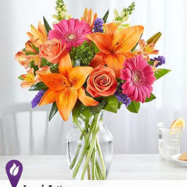 Bouquet of orange lilies, pink gerberas, and roses in a glass vase