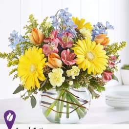 Mixed bouquet of yellow daisies, pink alstroemeria, and tulips in a glass vase