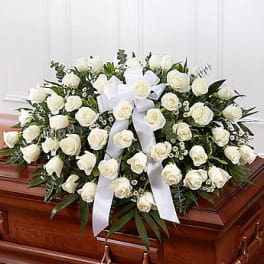 White rose casket spray with a white ribbon on a wooden casket
