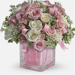 Pink and white roses arranged in a glass block vase with ribbon