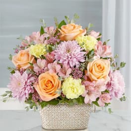 Peach roses and pink flowers arranged in a patterned basket