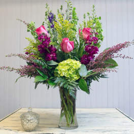 Tall bouquet of pink roses, purple blooms, and green hydrangea in a glass vase