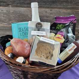 Gift basket filled with snacks, cookies, fruit, and a bottled drink in a wicker basket.