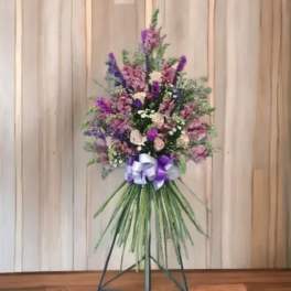 Tall standing floral spray with purple and pink flowers and a ribbon bow