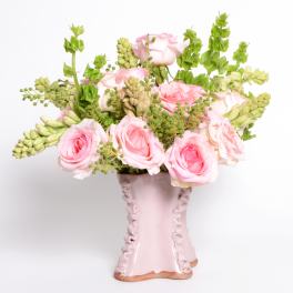 Pink roses and green filler flowers arranged in a pale pink vase