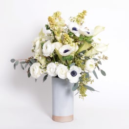 White floral arrangement in a tall gray vase with pale green accents