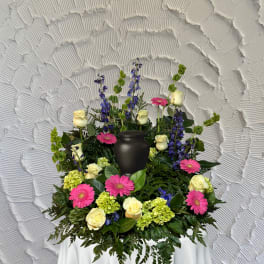 Floral funeral urn arrangement with pink gerberas, cream roses, and blue delphinium