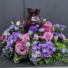 Purple and pink floral arrangement around a dark glass vase