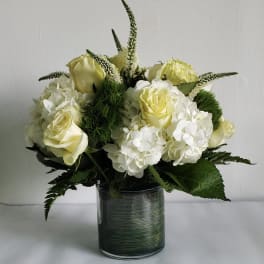 White and pale yellow roses with white hydrangeas in a glass vase
