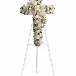 White floral cross arrangement on a stand with lilies and roses