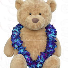 Tan teddy bear wearing a blue and purple flower lei