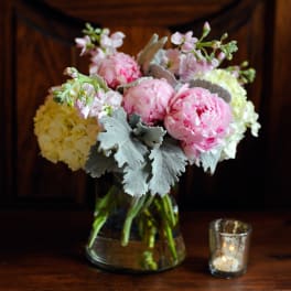 Pink peonies and pale hydrangeas in a glass vase with a small candle beside it