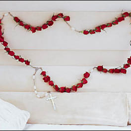 Red rose garland draped on a white upholstered headboard with a rosary cross