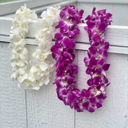 Two orchid leis draped over a white railing, one white and one purple.
