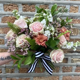 Hand-tied bouquet of pale pink roses, peach mums, and white blooms with a striped ribbon